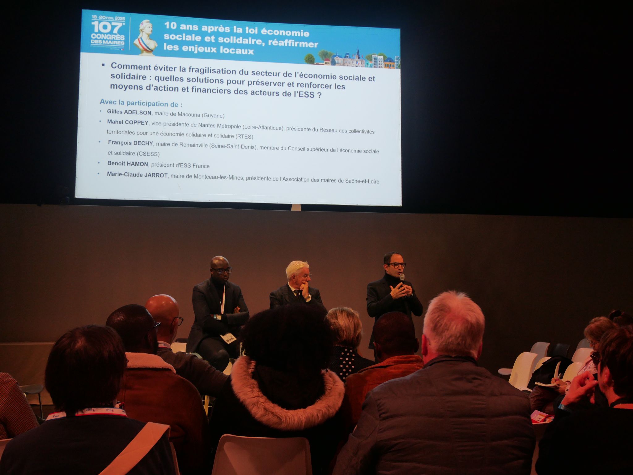 photo de trois hommes debout dans une salle de conférence, avec tout à droite benoit hamon au micro